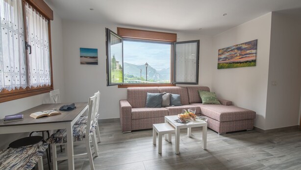 A cozy living room with a sofa, a dining table, and a view of mountains through a large window.