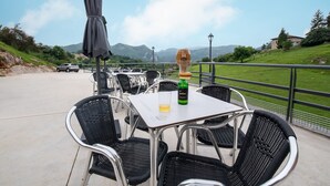 An outdoor dining area with metal chairs and tables, a bottle of Polian wine, and a view of green hills and mountains in the background.