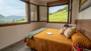 A bedroom with a large window offering a view of a green landscape and mountains.