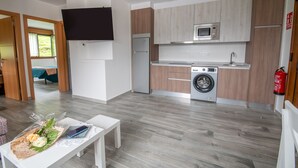 A modern kitchen with a microwave, oven, and washing machine. There is a TV mounted on the wall and a fire extinguisher on the wall.
