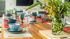 A dining table set with blue bowls, plates, and cutlery, a glass vase with green leaves, and a television in the background. - NEW! Stylish, Luxury Jungle Retreat with Saltwater Pool Samara Beach 5 mins (Sámara)