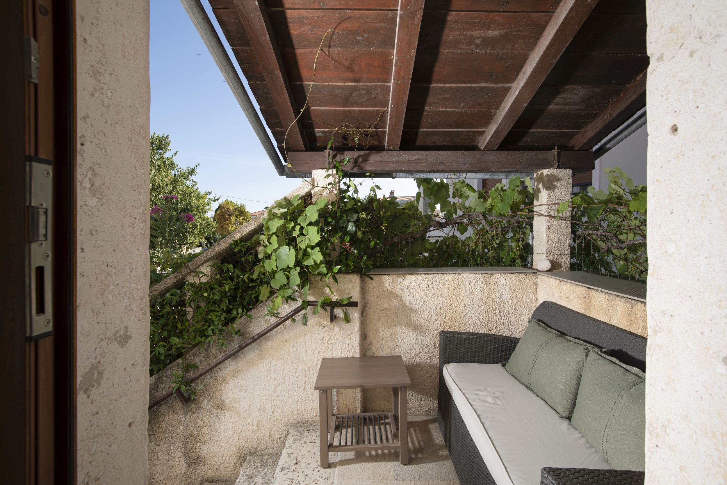 A covered outdoor seating area with a sofa and a small table, surrounded by a stone wall and greenery.
