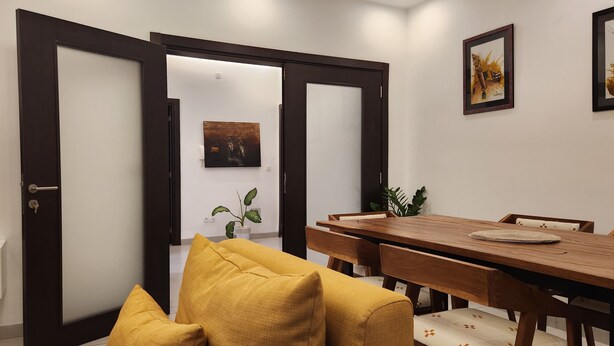 A modern dining area with a wooden table and chairs, a yellow sofa, and a framed artwork on the wall. - Superb Urban Oasis in Almadies
 (Dakar)