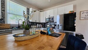 Une cuisine moderne avec des meubles blancs, un réfrigérateur noir et un ordinateur portable posé sur le plan de travail.