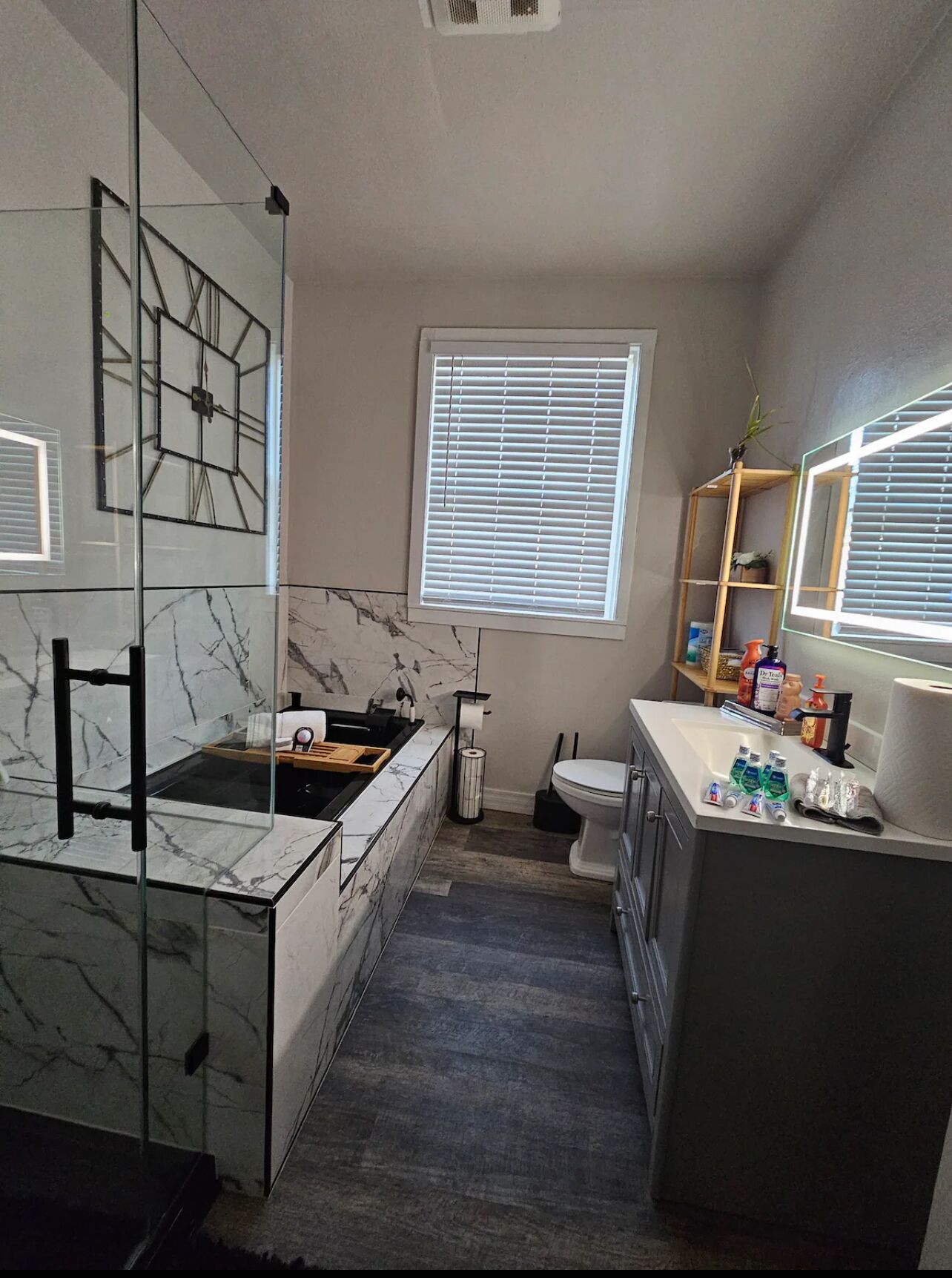 A modern bathroom with a glass shower enclosure, a marble-tiled vanity, and a window with blinds.