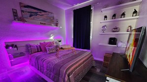Une chambre à coucher comprenant un lit, des tables de chevet, une télévision et des étagères ornées d’objets décoratifs.