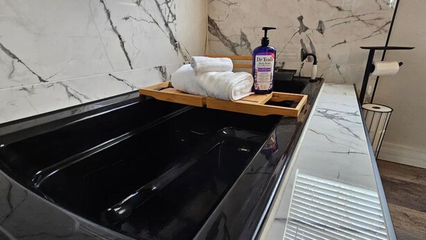 Un bain à remous doté d’un plateau en bois où sont posées des serviettes et une bouteille de gel douche de la marque Dr. Teal’s.