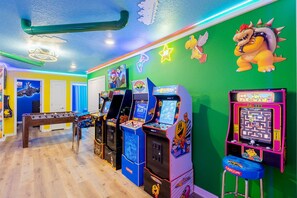 Uma sala de jogos bem iluminada com várias máquinas de jogos, uma mesa de futebol de mesa e decorações coloridas nas paredes.