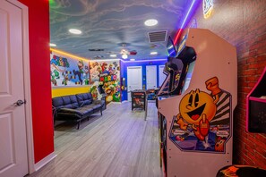 Una habitación con un mural de Mario, un sofá de cuero negro, una consola de videojuegos y una pared de ladrillo.