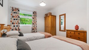 A bedroom with two beds, a wooden wardrobe, a mirror, and a window with curtains. - St Helens Apartment 2 - Short Walk to Beach (Wisemans Bridge)