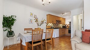 A modern kitchen with wooden cabinets, a dining table with chairs, and a potted plant. - St Helens Apartment 2 - Short Walk to Beach (Wisemans Bridge)