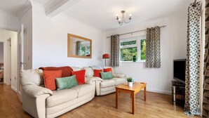 A living room with a beige sofa, a wooden coffee table, and a TV. - St Helens Apartment 2 - Short Walk to Beach (Wisemans Bridge)