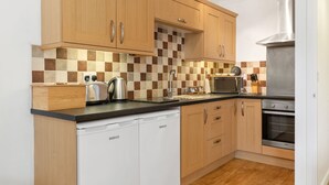 A modern kitchen with wooden cabinets, a microwave, a toaster, and a dishwasher. - St Helens Apartment 2 - Short Walk to Beach (Wisemans Bridge)
