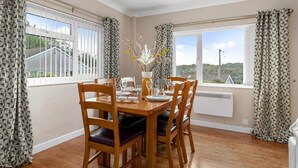Uma sala de jantar com mesa de madeira preparada para quatro pessoas, rodeada por cadeiras com assentos acolchoados.