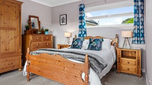 Quarto com cama de madeira, duas mesas de cabeceira com luminárias, cômoda e janela com cortinas.