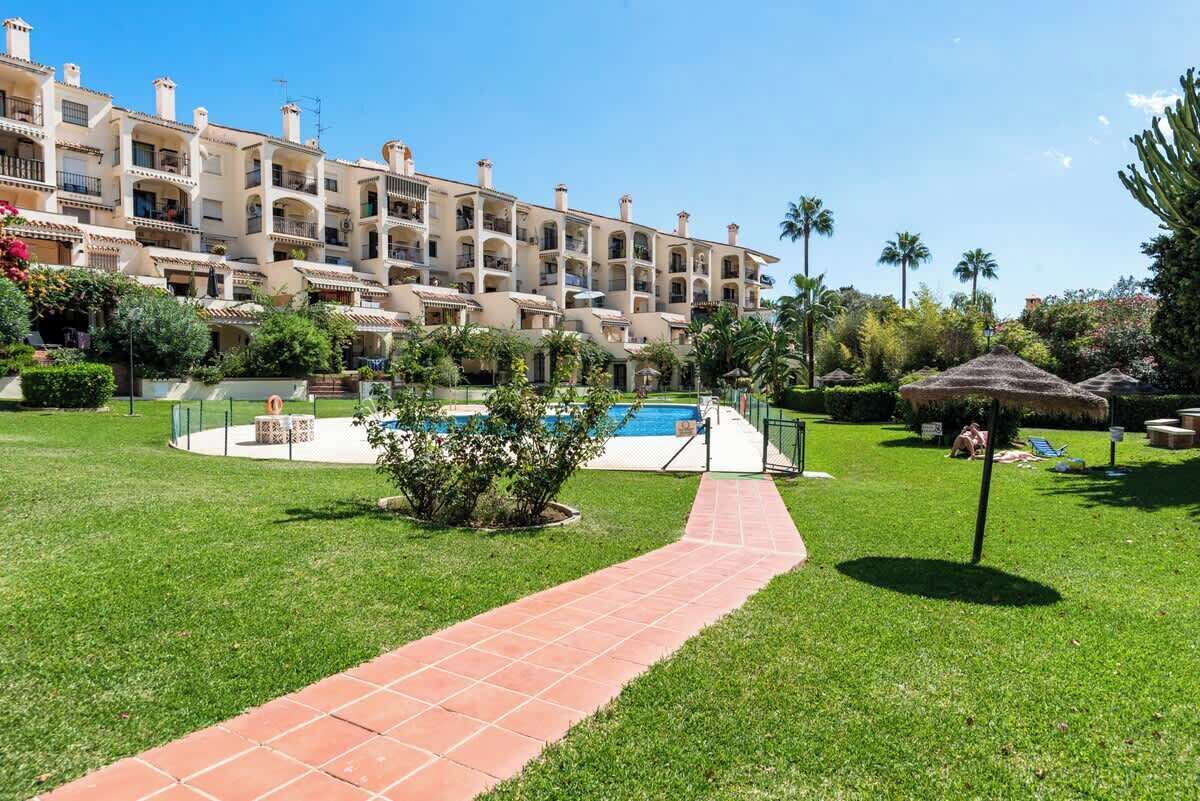 A hotel with a swimming pool, a garden with a paved walkway, and palm trees.