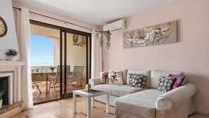 A living room with a sofa, a coffee table, and a fireplace. There is a sliding glass door leading to an outdoor area with a table and chairs. - Zeus Apartment Riviera del Sol by Costarentals - Ref 221 (Mijas)