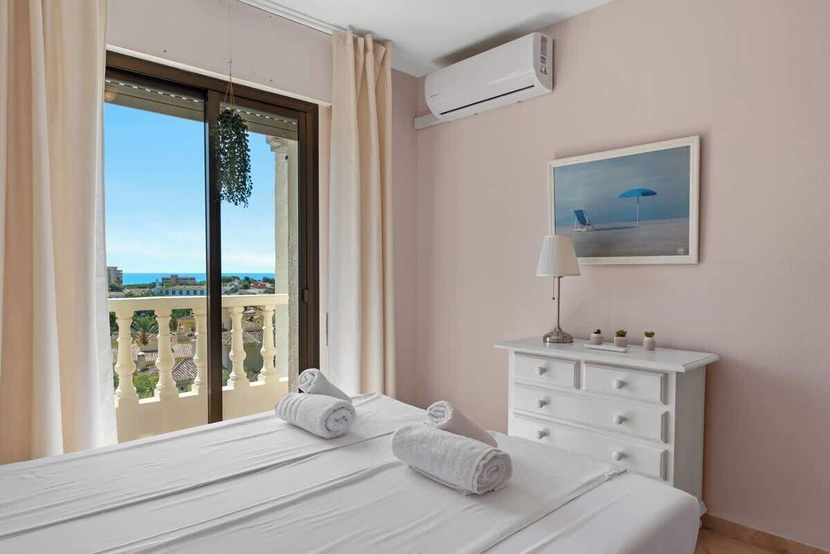A hotel room with a balcony, a bed with towels, a white dresser, and a painting.