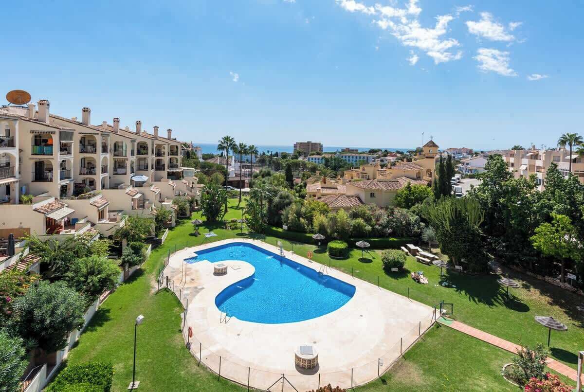 A resort with a large swimming pool, lush greenery, and a view of the sea.