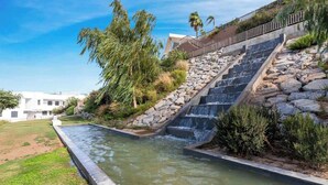 A water feature with cascading steps and a stone wall, surrounded by greenery and a clear sky. - Casa Banderas Pool & Gym by Costarentals - Ref 237 (La Cala de Mijas)