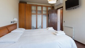 Een hotelkamer met een groot bed, een houten garderobe, een aan de muur bevestigde televisie en een radiator.