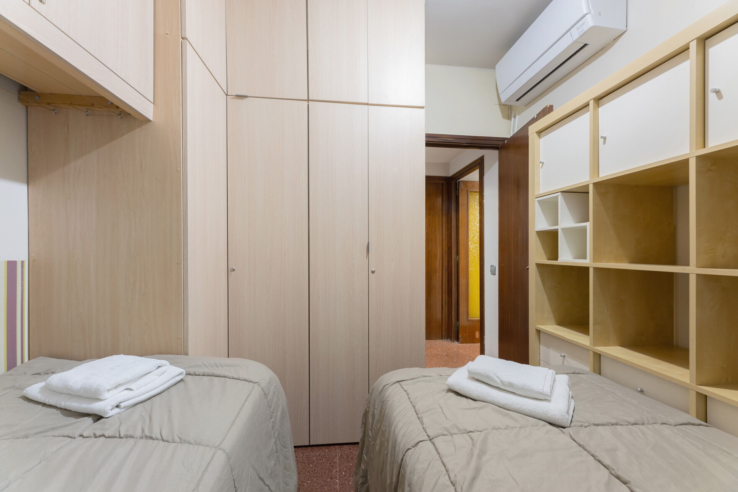 Ein Hotelzimmer mit zwei Betten, einem Kleiderschrank und einer fest eingebauten Ablagefläche.