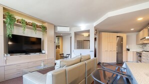 Een moderne woonkamer met een flatscreen televisie, een beige bank en een eethoek met een metalen bar.