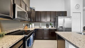 Une cuisine moderne avec des meubles de couleur sombre, des appareils en acier inoxydable, des comptoirs en granit et une horloge au mur.