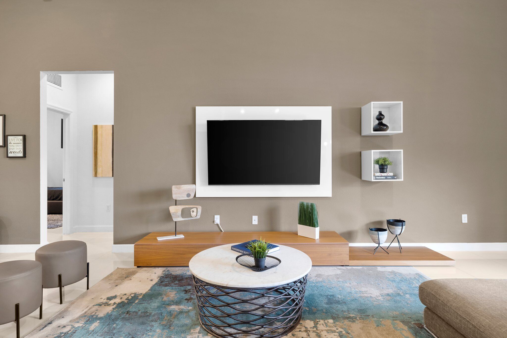 A modern living room with a large flat-screen TV mounted on the wall, a round coffee table with a plant, and a minimalist decor style.