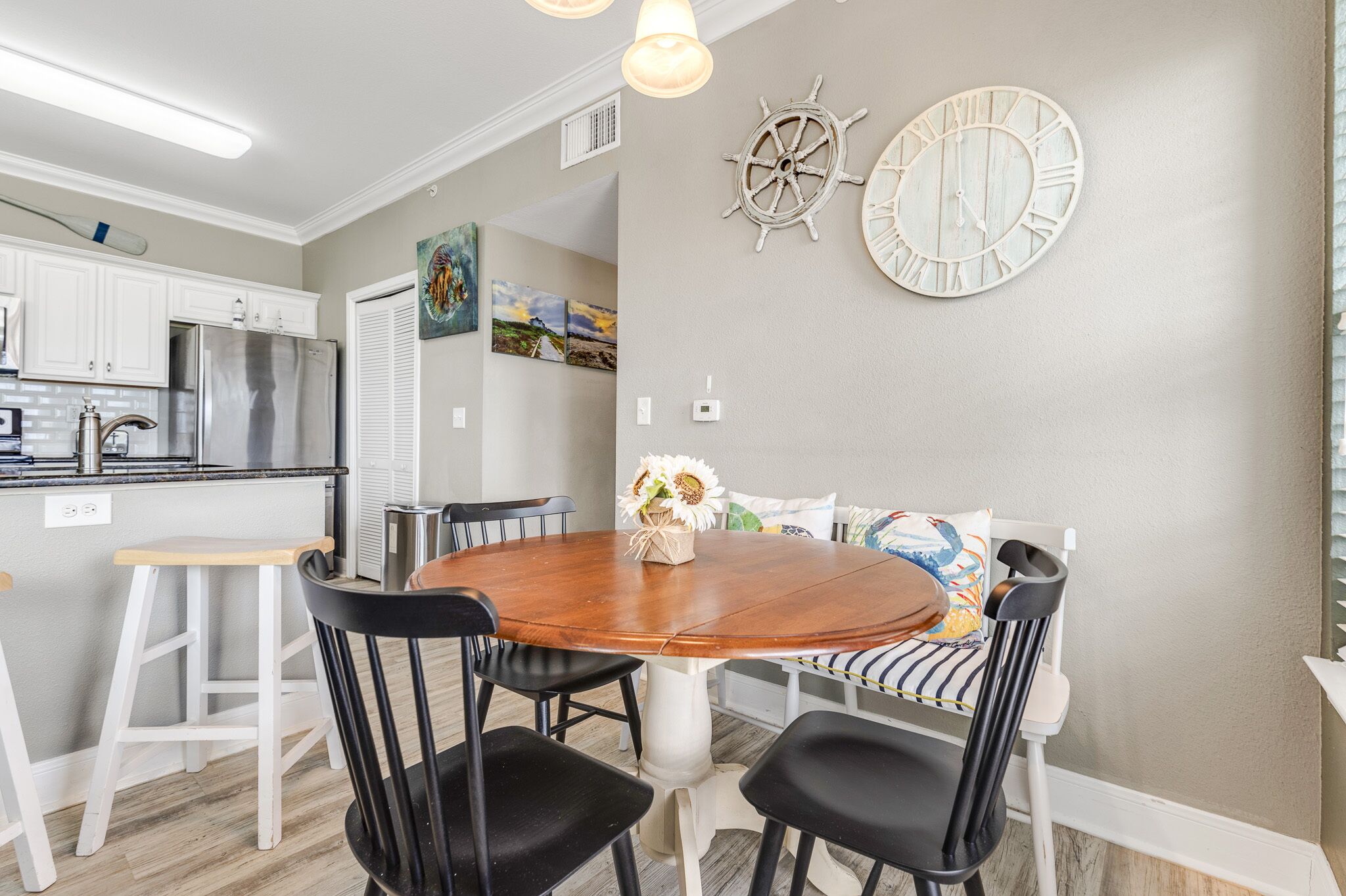A dining area with a round wooden table, black chairs, and a white pedestal base. There are two wall-mounted clocks and a decorative wall piece.