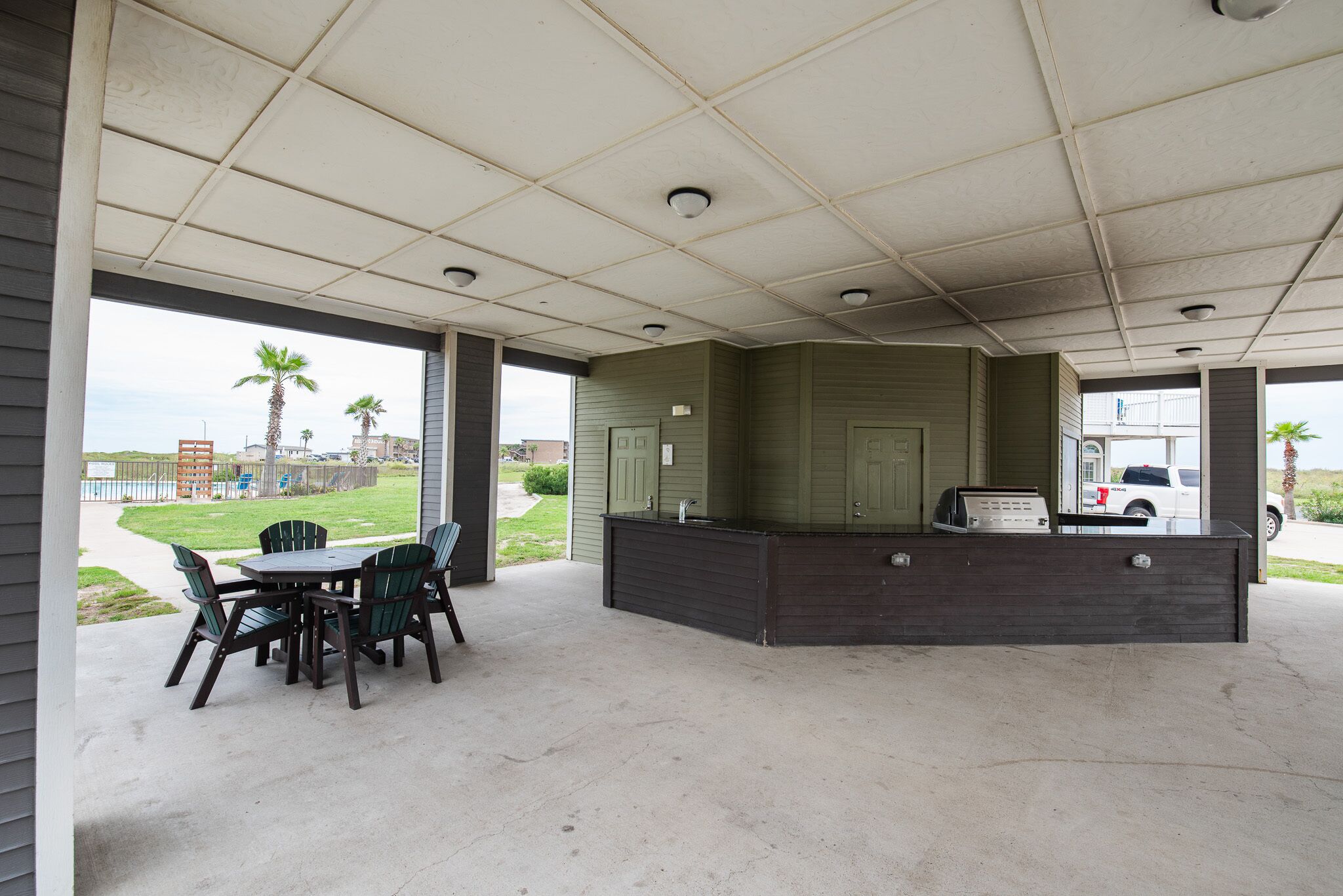 A covered outdoor area with a concrete floor, a table with chairs, and a counter with a sink.