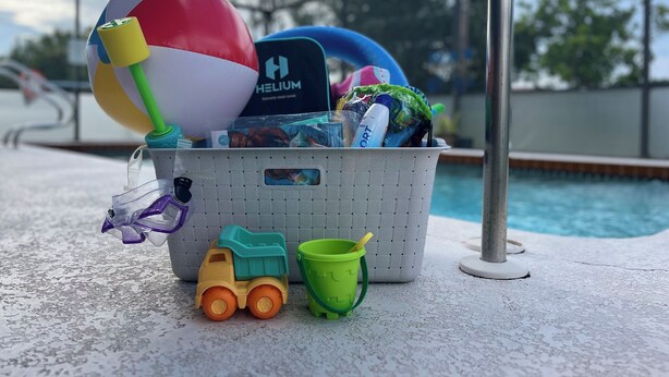 Un espace aménagé au bord de la piscine, avec un seau contenant un ballon de plage, un camion jouet et un gobelet vert.