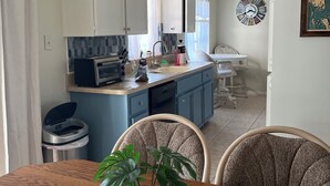 Une cuisine moderne avec des meubles bleus, une table à manger en bois agrémentée d’une plante en pot et un luminaire suspendu.