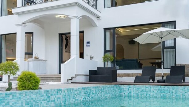 Un bâtiment moderne doté d’un espace piscine, comprenant des chaises longues et un parasol.