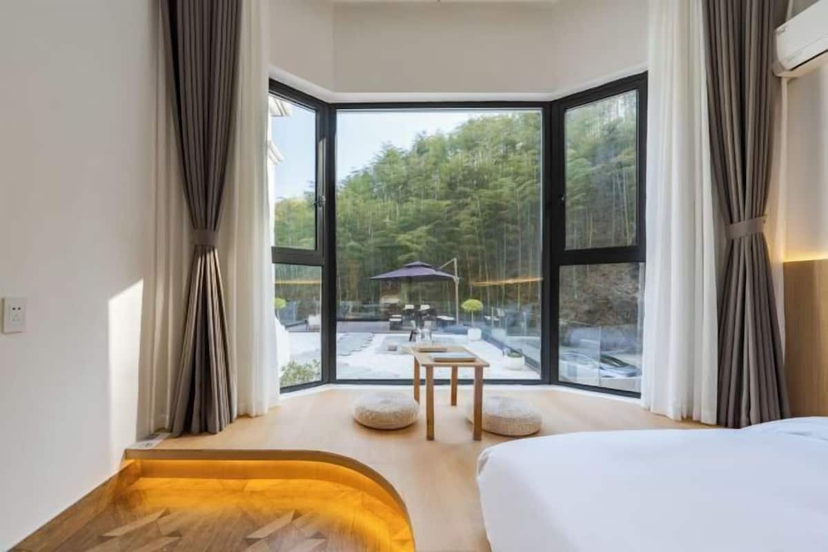 A modern room with a large window, a bed, a small table, and a bench.