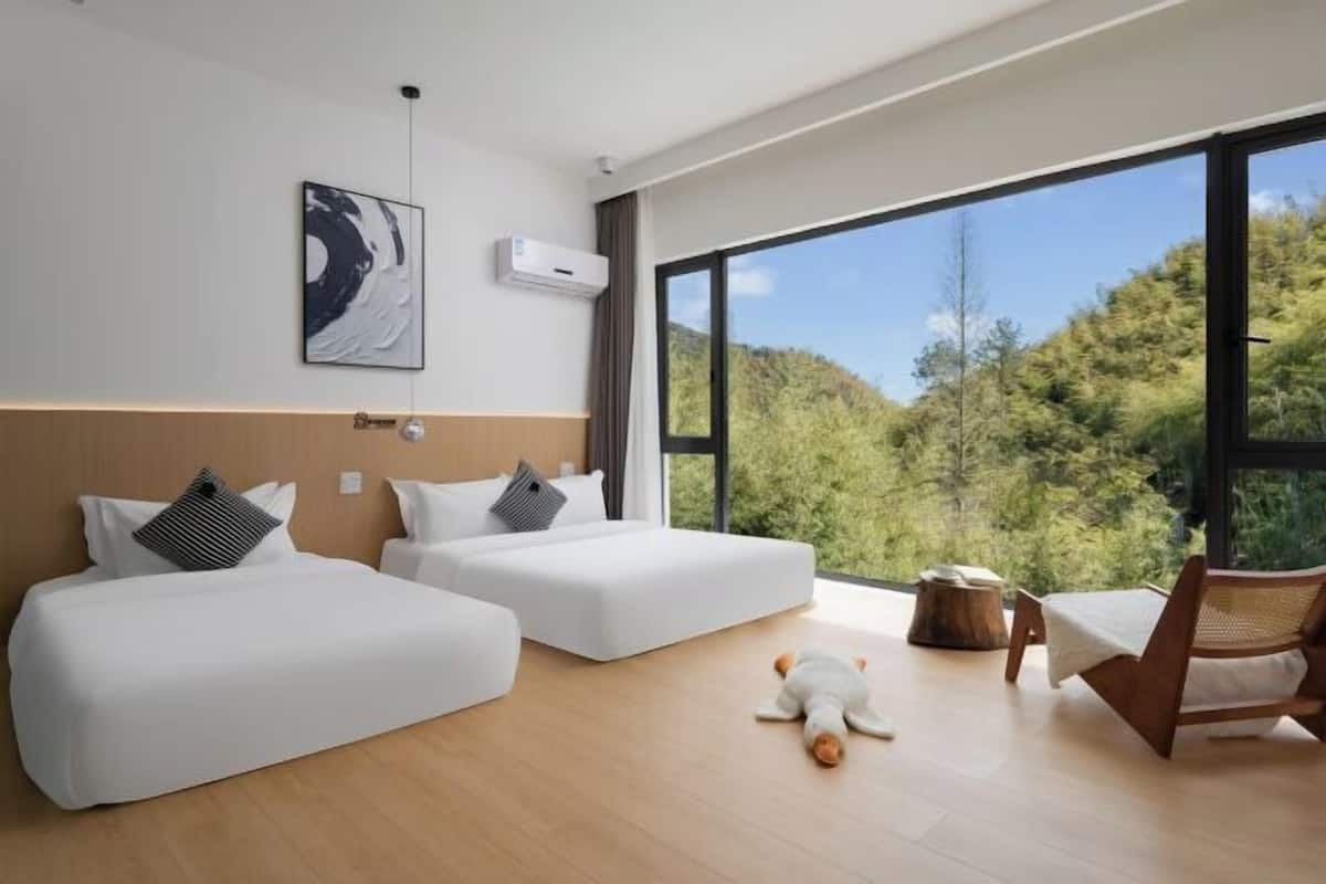 A modern hotel room with two beds, a large window, and a view of the outdoors.