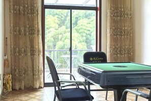 A billiards table with a green felt surface, a black cushioned chair, and a view of a balcony with a glass door. - Yundan Fengqing Inn (Deqing)