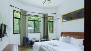 Une chambre d’hôtel avec un grand lit, un bureau, deux chaises, une télévision et une fenêtre avec des rideaux.