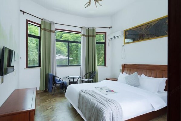 A hotel room with a large bed, a desk, two chairs, a television, and a window with curtains. - Yundan Fengqing Inn (Deqing)