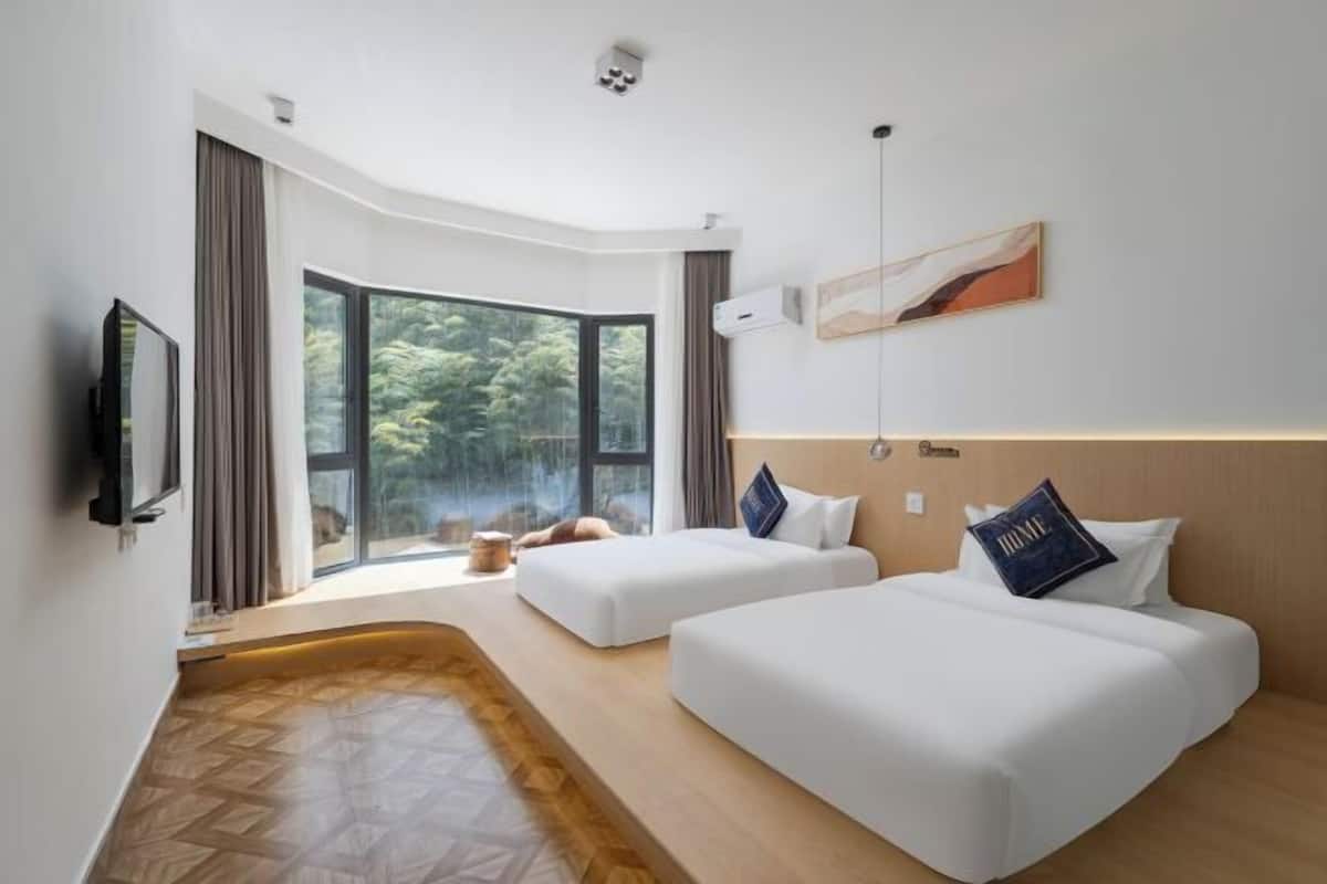 A hotel room with two beds, a TV, a large window, and a wooden floor.
