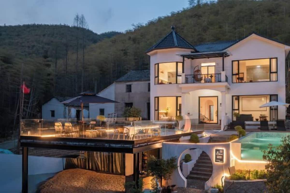 A modern two-story house with a balcony, a swimming pool, and a well-lit outdoor area.