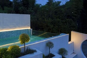 A modern outdoor pool area with a glass barrier, surrounded by white walls and greenery. - Yundan Fengqing Inn (Deqing)