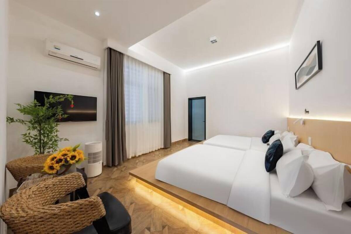 A modern hotel room with a large bed, a TV, a desk with a chair, and a plant.