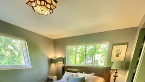 A bedroom with a large bed, two bedside lamps, a rug, and a window with a view of trees.