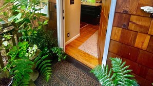 A wooden exterior with a welcome mat, potted plants, and a framed picture.