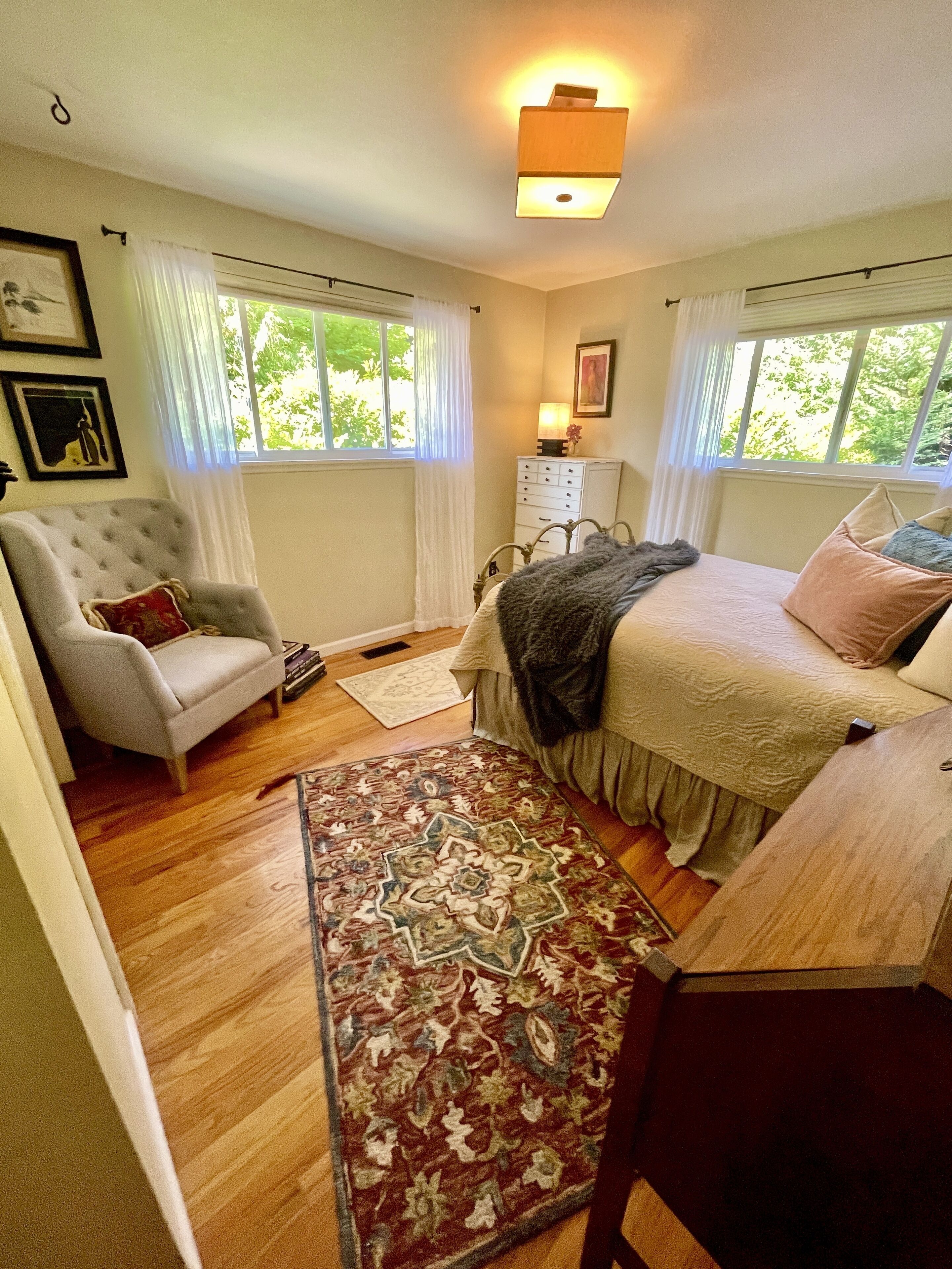 A bedroom with a bed, a chair, a nightstand, a lamp, and a window with curtains.