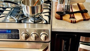 A kitchen with a stainless steel stove, a digital clock, and various cooking utensils on the counter.