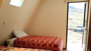 A bedroom with two beds, a skylight, and a view of a rural landscape through a door. - APU TACLLO LODGE (Layo)