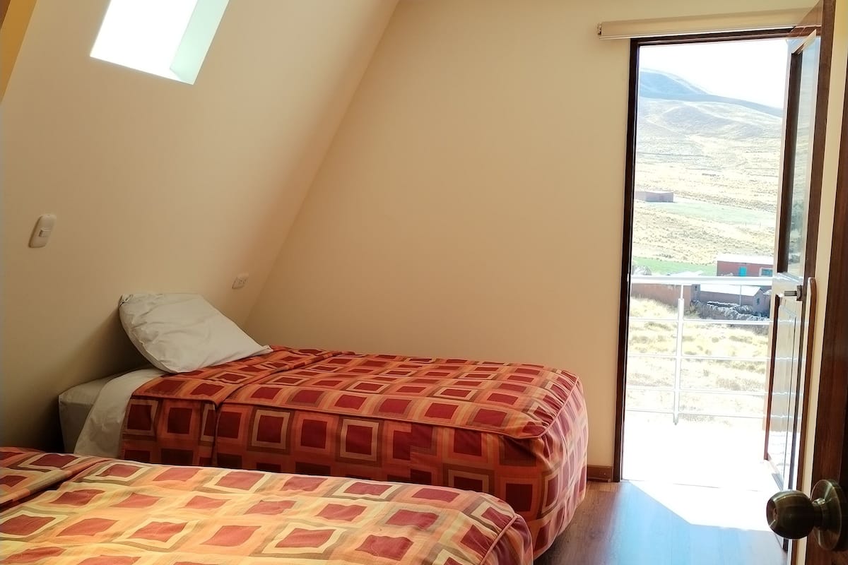 Une chambre avec deux lits, une lucarne et une vue sur un paysage rural, visible à travers une porte.