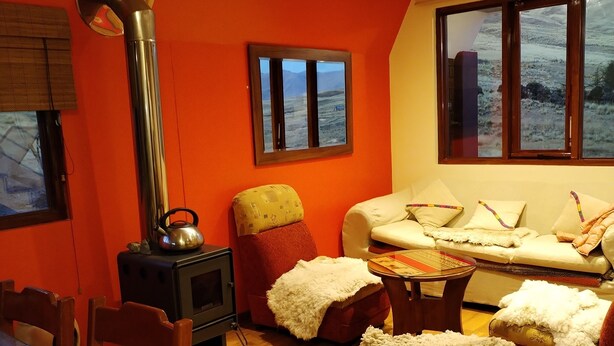 A cozy living room with a wood-burning stove, a sofa set, and a dining area with wooden furniture. - APU TACLLO LODGE (Layo)
